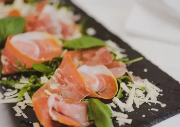 Frische Antipasti mit Prosciutto, Basilikum und Parmesan im Ristorante Ciao in München nahe Au-Haidhausen, serviert auf einer Schieferplatte.