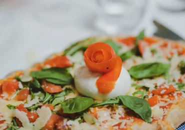 Frische Burrata-Pizza mit Basilikum, Tomaten und dekorativer Gemüseblüte im Ristorante Ciao in München nahe Giesing.
