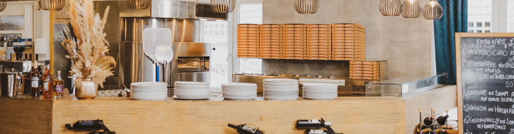 Offene Pizzastation mit Pizzaofen, gestapelten Pizzakartons und gedeckter Theke im Ristorante Ciao in München.