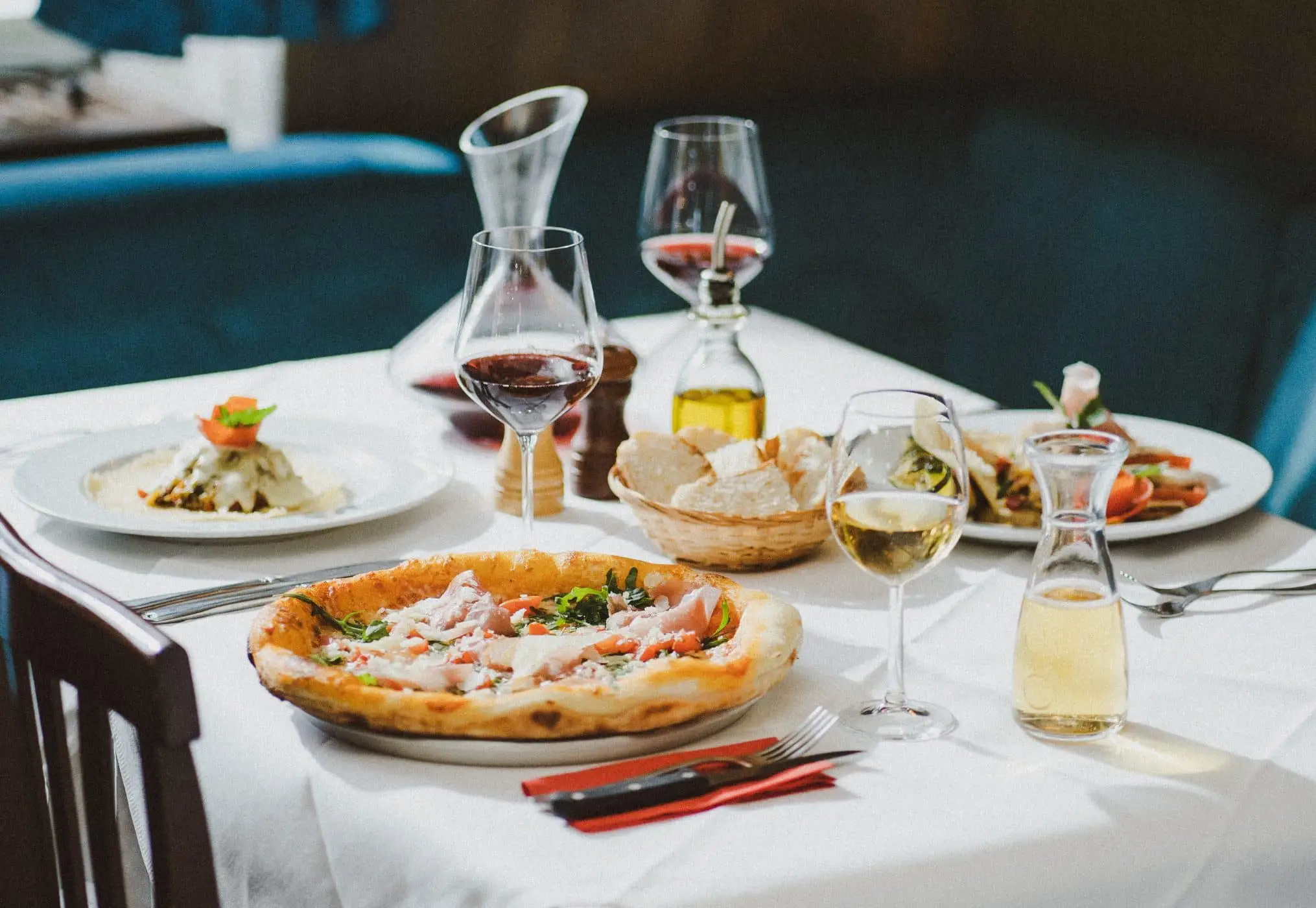 Italienische Speisen wie Pizza, Antipasti und Wein auf einem elegant gedeckten Tisch im Ristorante Ciao in München nahe Ostbahnhof.